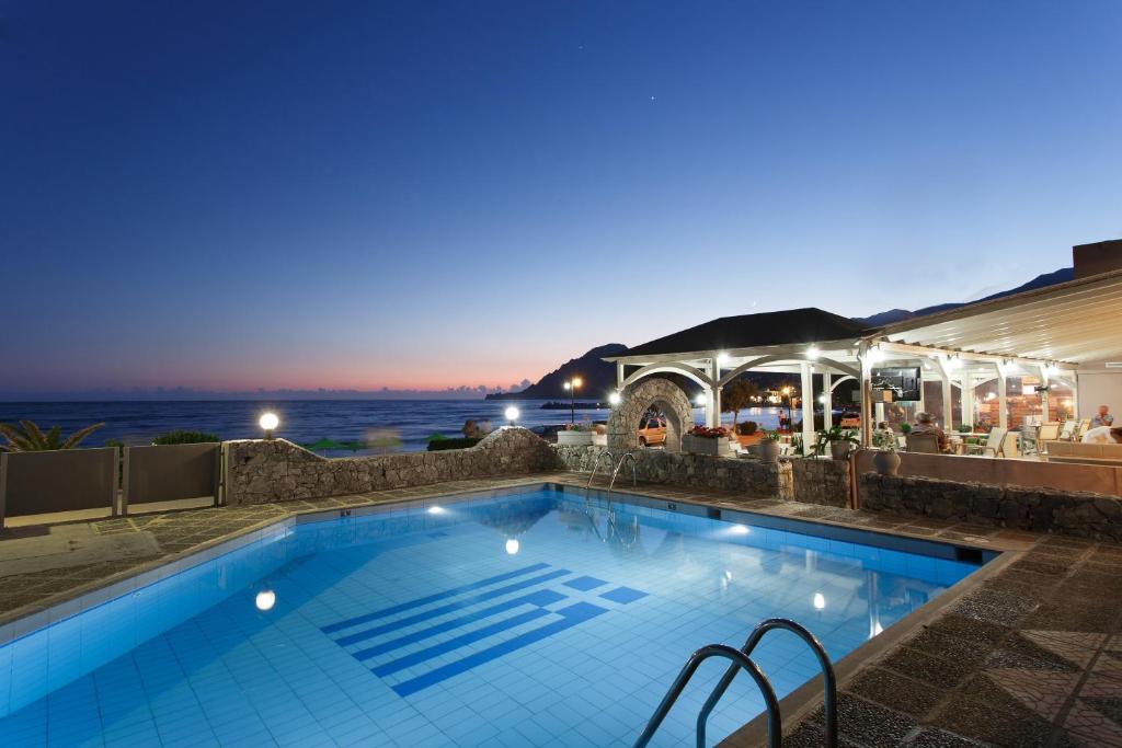 a swimming pool at night with the ocean in the background at Lamon Hotel in Plakias