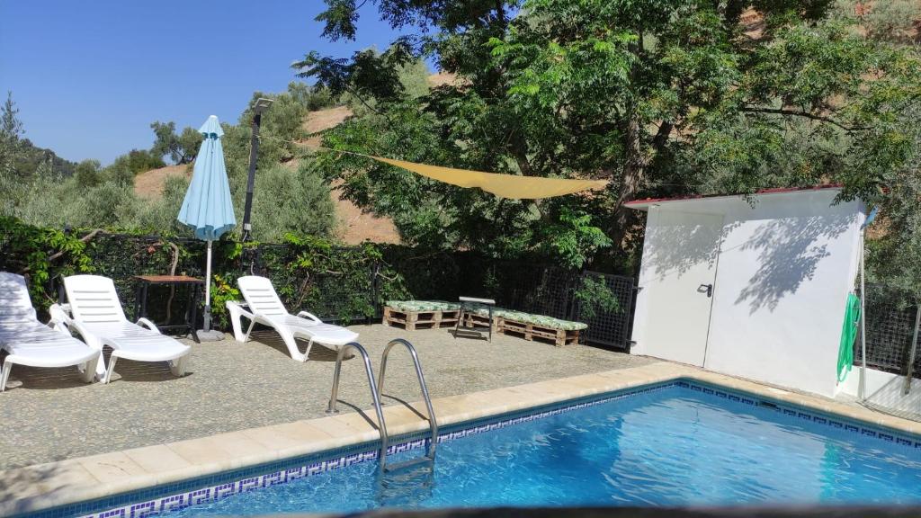 a swimming pool with chairs and a table and an umbrella at Casa Rural Los Angostones in Villanueva del Arzobispo