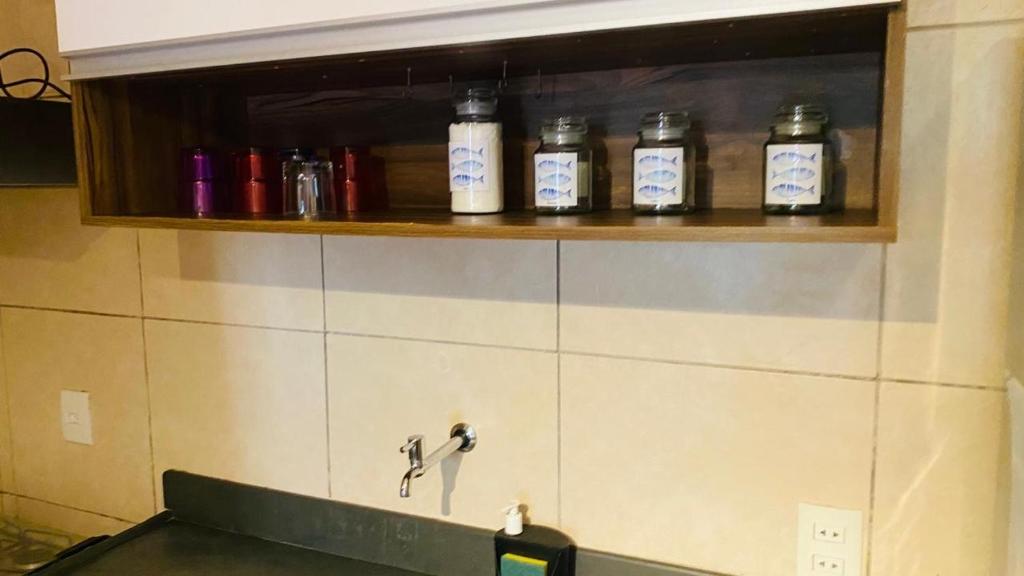 a row of bottles on a shelf above a sink at Duplex no Centrinho de Pipa cozinha e 2 banheiros in Pipa
