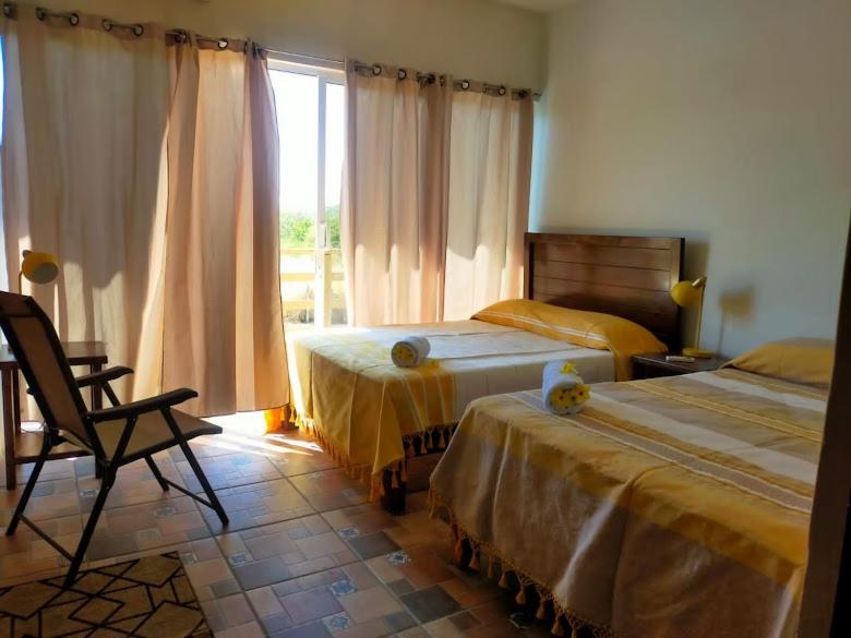 sypialnia z dwoma łóżkami, krzesłem i oknem w obiekcie Casa Villa NOA w mieście Puerto Escondido