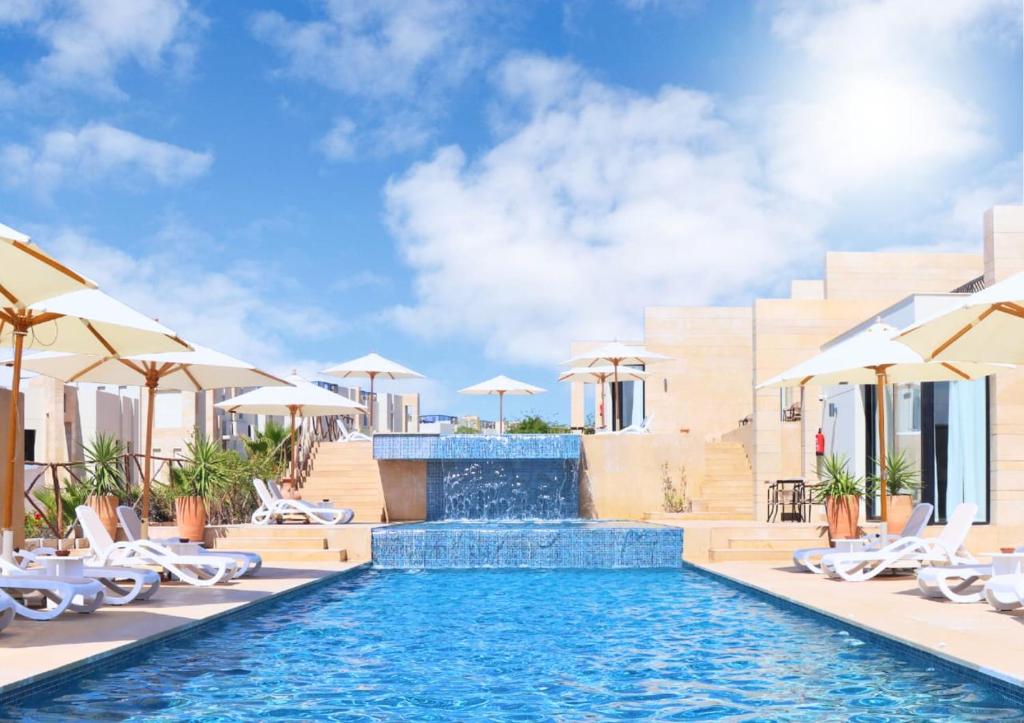 a pool at a resort with chairs and umbrellas at Med IL Caesar ADULT ONLY in Zāwiyat al ‘Awwāmah