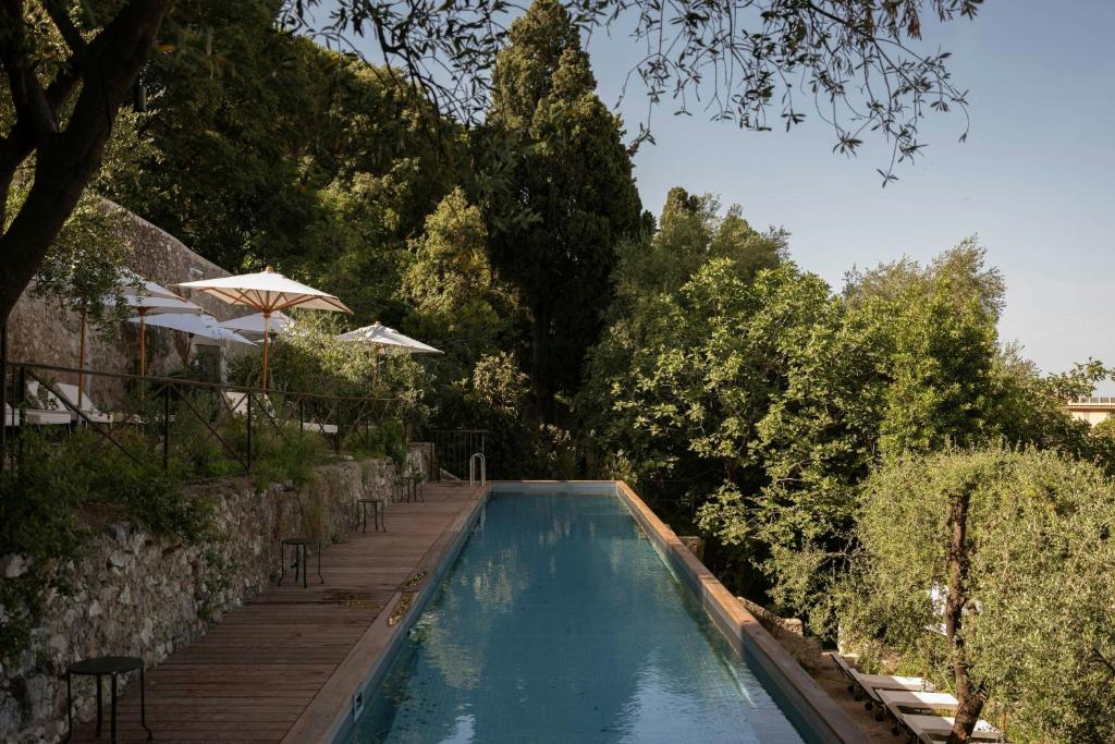 a swimming pool with chairs and an umbrella and trees at Hôtel du Couvent, a Luxury Collection Hotel, Nice in Nice