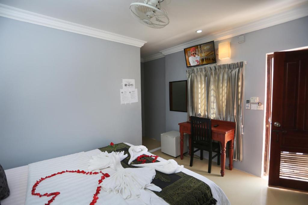 a bedroom with a bed with white sheets and a desk at Cheng Lay Guesthouse in Siem Reap
