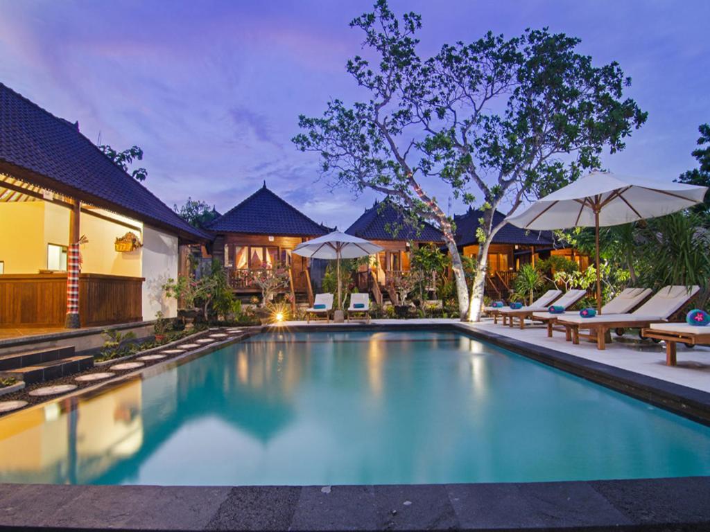 a pool with chairs and umbrellas next to a house at Cassava Bungalow in Nusa Lembongan