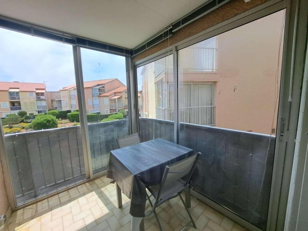 d'une table et de chaises sur un balcon avec fenêtres. dans l'établissement Appartement 2 pièces avec loggia aménagée à Marseillan-Plage - FR-1-326-863, à Marseillan