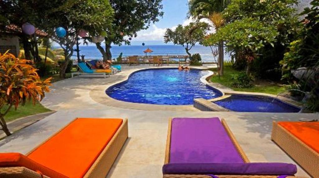 a swimming pool with two purple and orange chairs and the ocean at Relax Beach Resort Candidasa in Candidasa