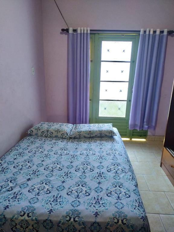 a bedroom with a bed and a window with purple curtains at Espaço Sinara in Jaraguá