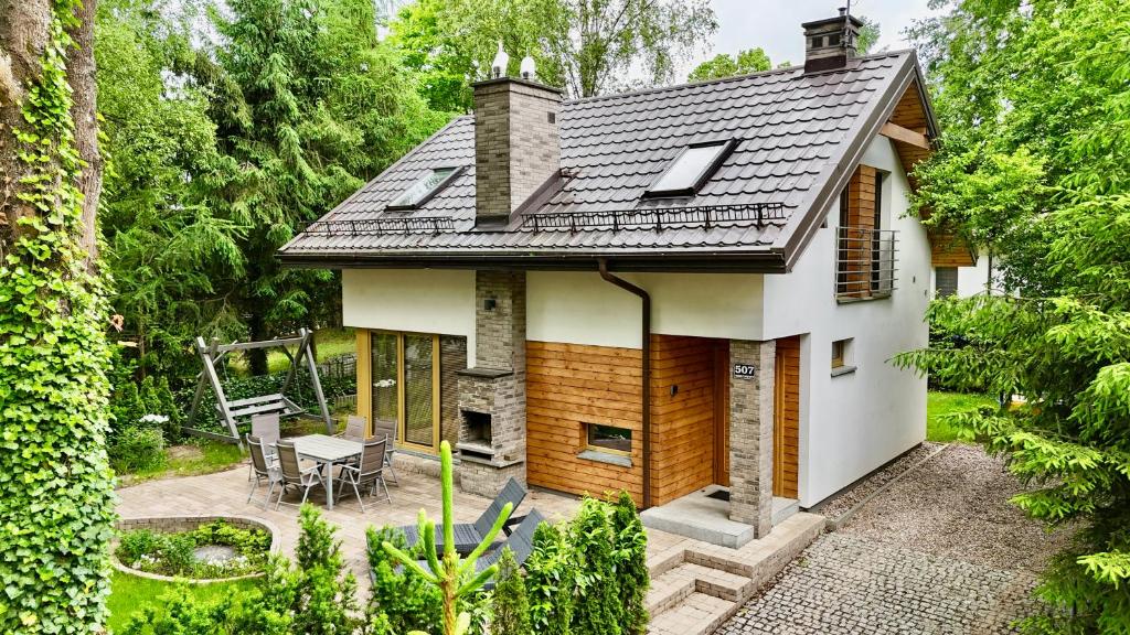 a small white house with a fireplace in a garden at Mazursko - komfortowe domy 8 osobowe nad jeziorem, balia lub sauna in Kretowiny
