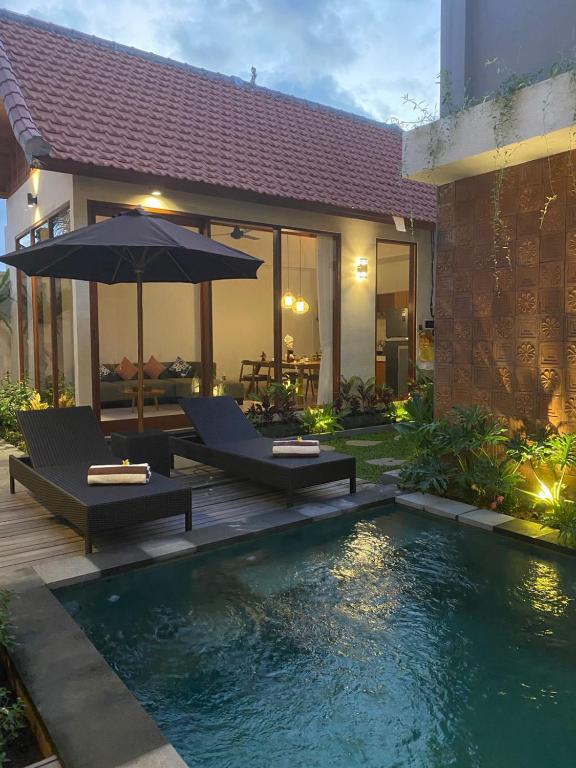 a pool with two chairs and an umbrella next to a house at Dream House Ubud in Ubud