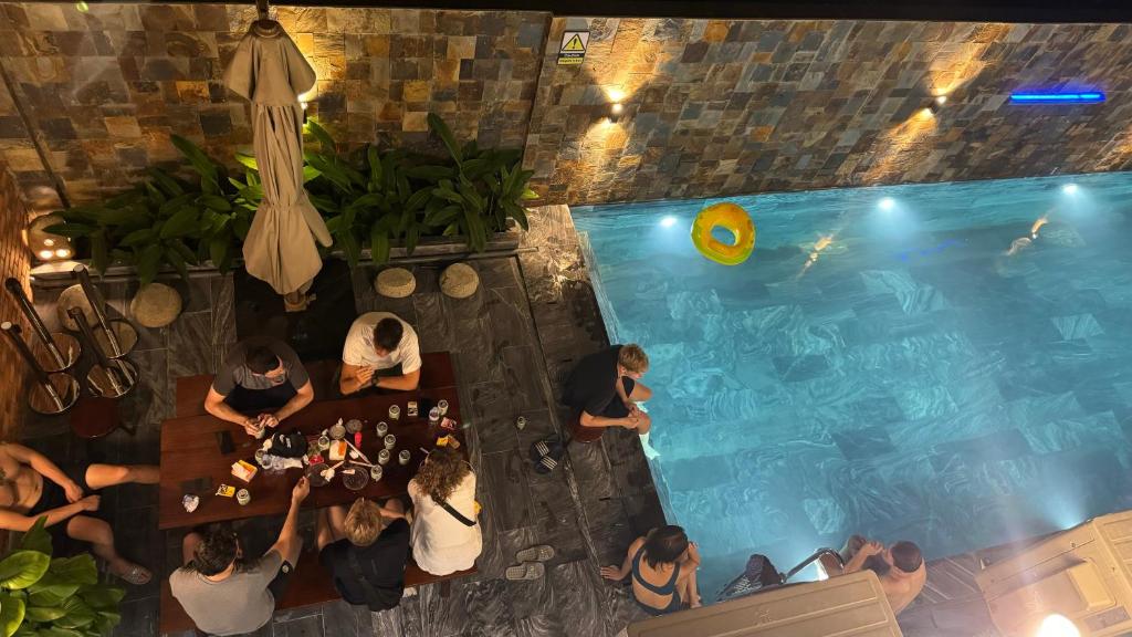 a group of people sitting at a table near a swimming pool at Ha Giang Backpacker Hostel in Làng Me