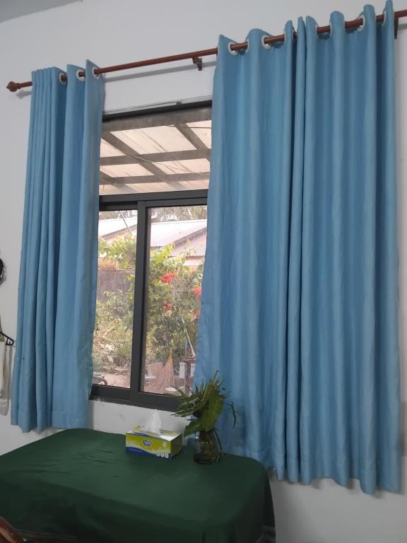 Una ventana con cortinas azules junto a una mesa verde. en Herotus Local House near Beach, en Phu Quoc
