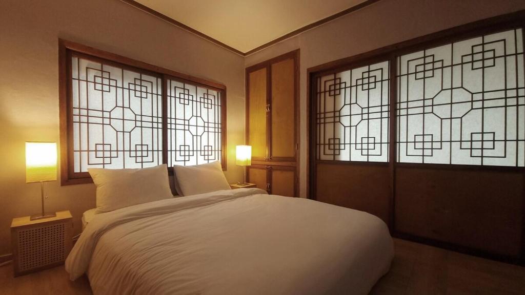 a bedroom with a white bed and two windows at Haenarr Hanok Stay in Mandarin Orchard, 100m from Sea in Seogwipo