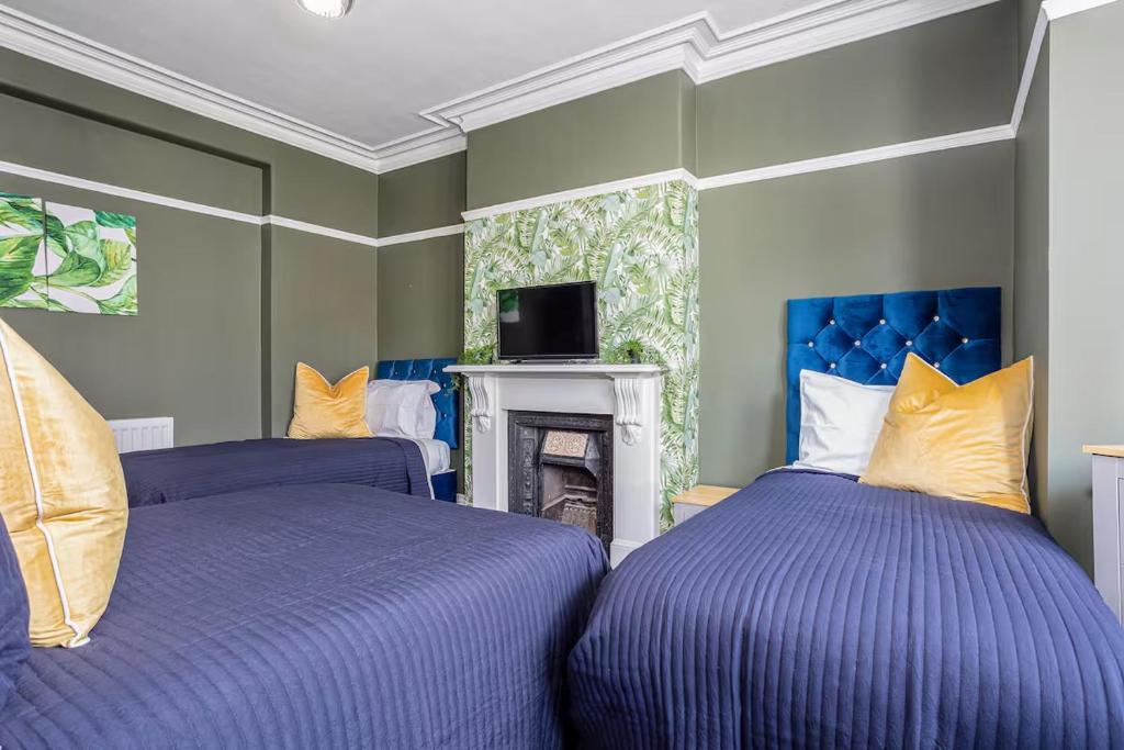 two beds in a room with blue and yellow pillows at Room 3 plus optional additional lounge area with double sofa bed, 23 Deganwy Avenue in Llandudno