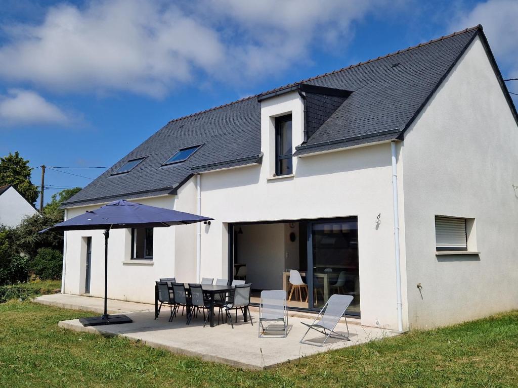 une maison blanche avec une table, des chaises et un parasol dans l'établissement Maison moderne pour 8 pers. à 600m de la plage avec grand jardin - FR-1-639-140, à Sarzeau