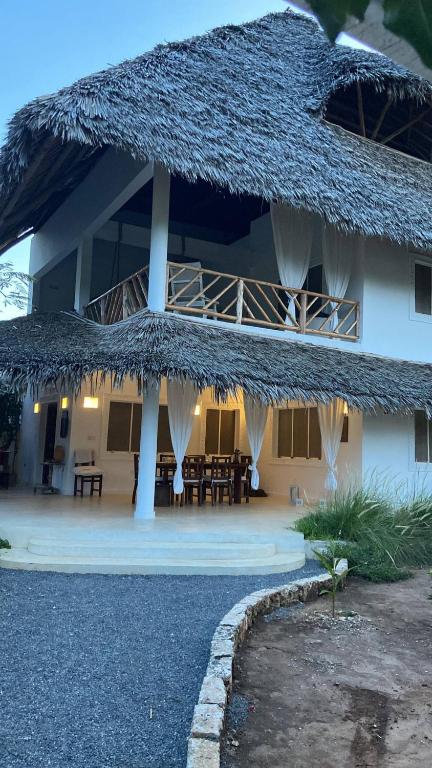 a building with a straw roof with tables and chairs at Nyumba ya Bubi in Watamu