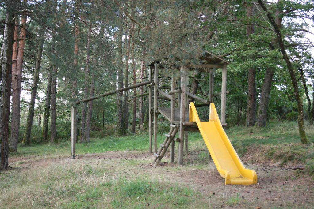 a playground with a yellow slide in the woods at La Ptite Ferme de Caro in Meyrignac-lʼÉglise