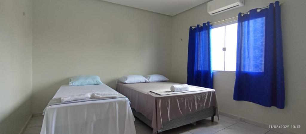 a room with two beds and a window with blue curtains at A M Hotel in São Luís