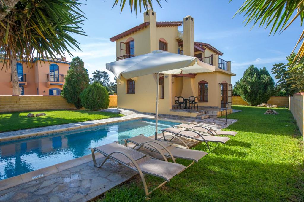 a pool with chairs and an umbrella next to a house at Ferienhaus In Polis Chrysochous Mit Offenem Kamin in Polis Chrysochous