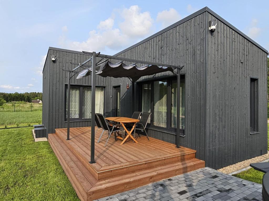 a black house with a wooden deck with a table at Budas in Plieņciems
