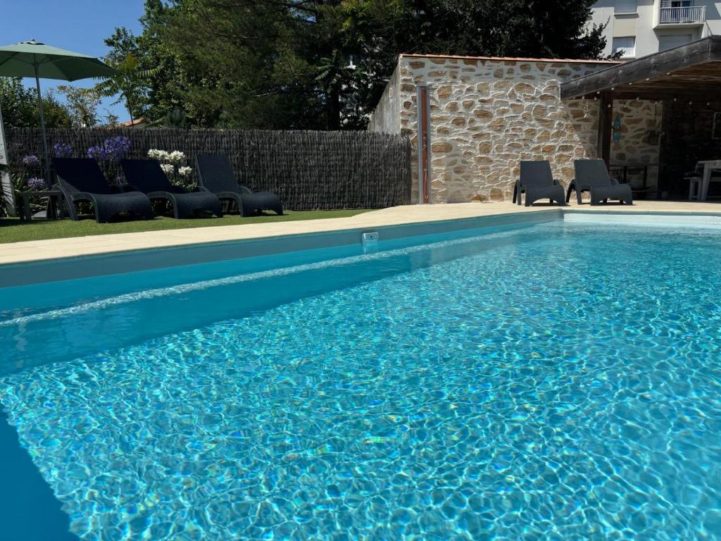 - une piscine bleue avec des chaises et un parasol dans l'établissement Gîte Villa la Garenne Ctre ville St Jean de Monts, à Saint-Jean-de-Monts