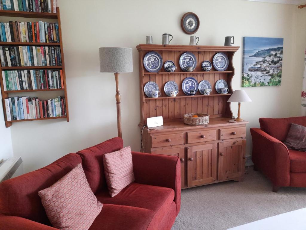 a living room with two red chairs and a book shelf at Jordan Cottage in Fowey