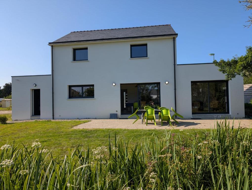 une maison blanche avec des chaises vertes devant elle dans l'établissement Maison familiale design proche plage draps fournis, à Étel