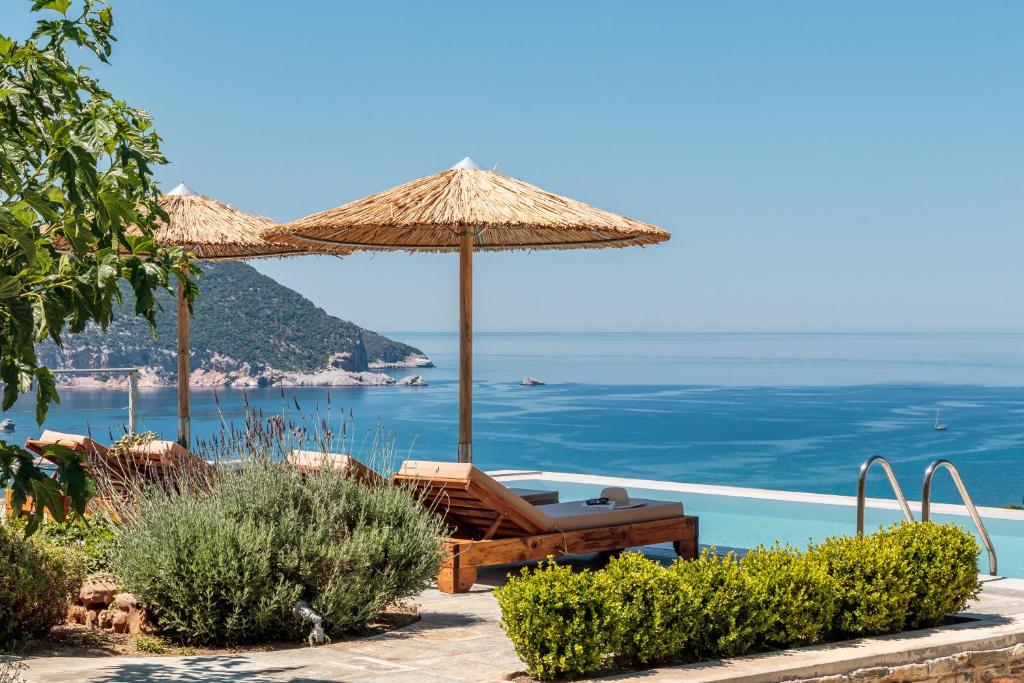 a bench under an umbrella next to the ocean at Villa Myli - Skopelos in Skopelos Town
