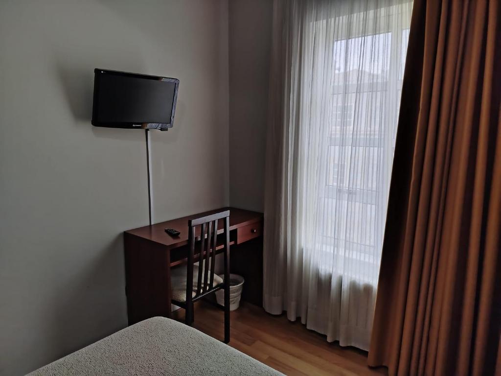 a bedroom with a desk and a television and a window at Hotel Camiño de Santiago in Val do Dubra