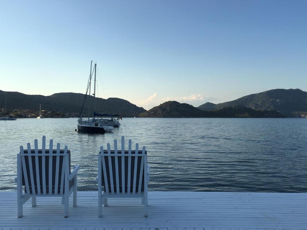 two chairs on a dock with a boat in the water at Beyaz İskele Hotel & Restaurant in Selimiye