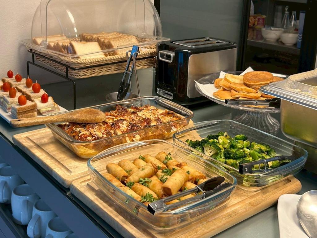 A buffet display of baked dishes, spring rolls, broccoli, pastries, and pancakes.