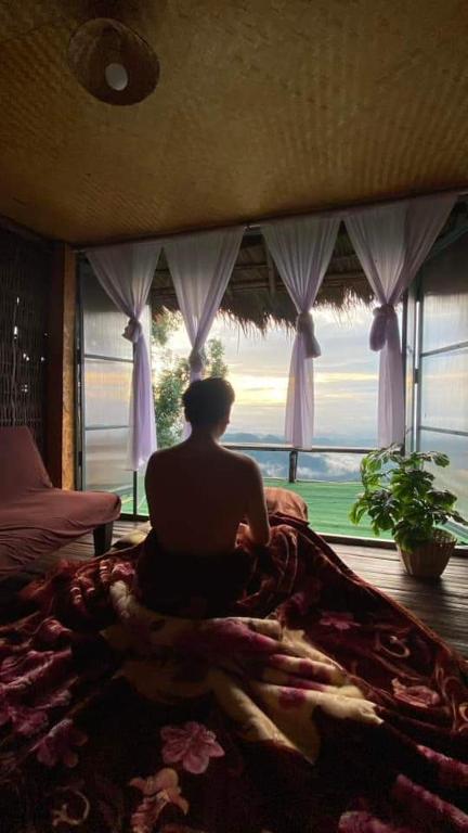 a man sitting on a bed in front of a window at ASA Private Homestay - บ้านนายพราน แนววินเทจ in Ban Huai Khai