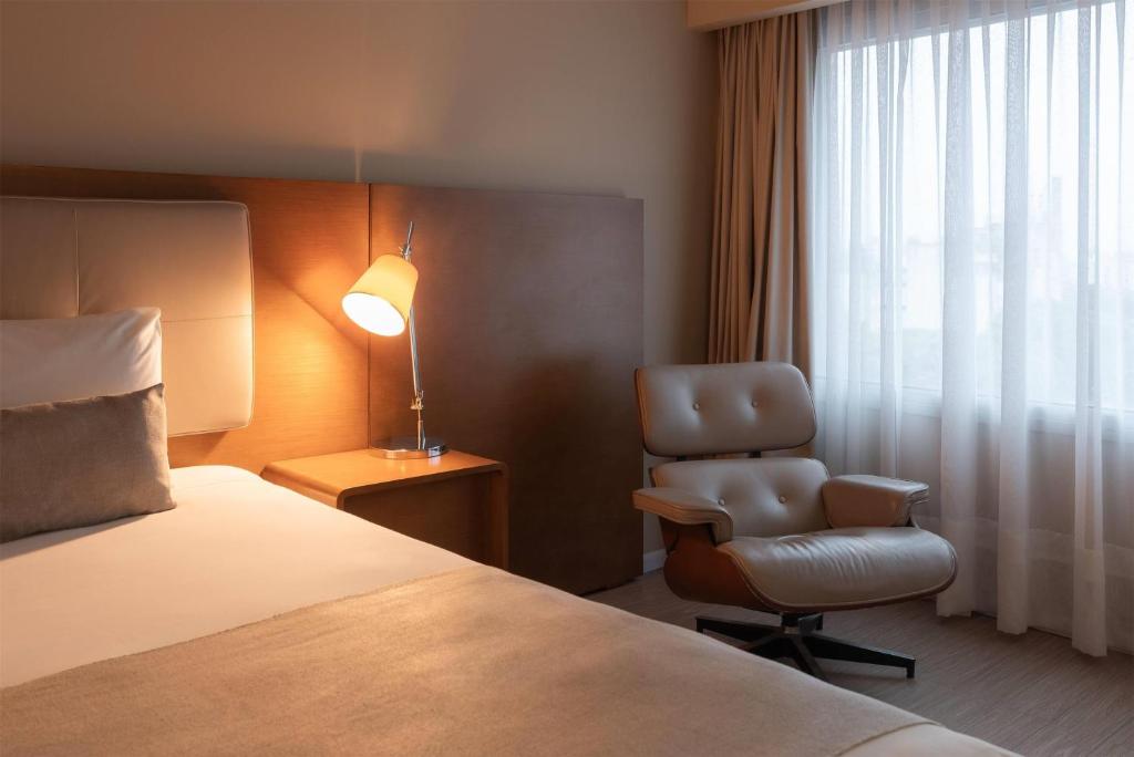 a hotel room with a bed and a chair and a lamp at Dazzler by Wyndham Montevideo in Montevideo