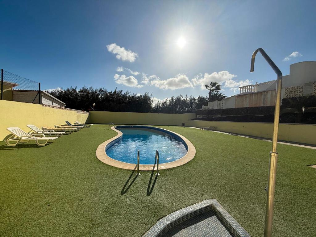 a swimming pool on a lawn with chairs on it at Fuerte Casa 66 in Costa Calma