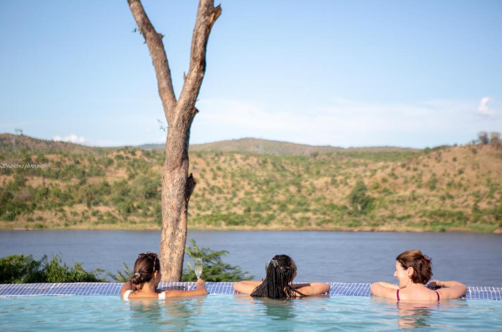 three women sitting in a swimming pool next to a lake at Zua Safari Lodge in Chikwawa