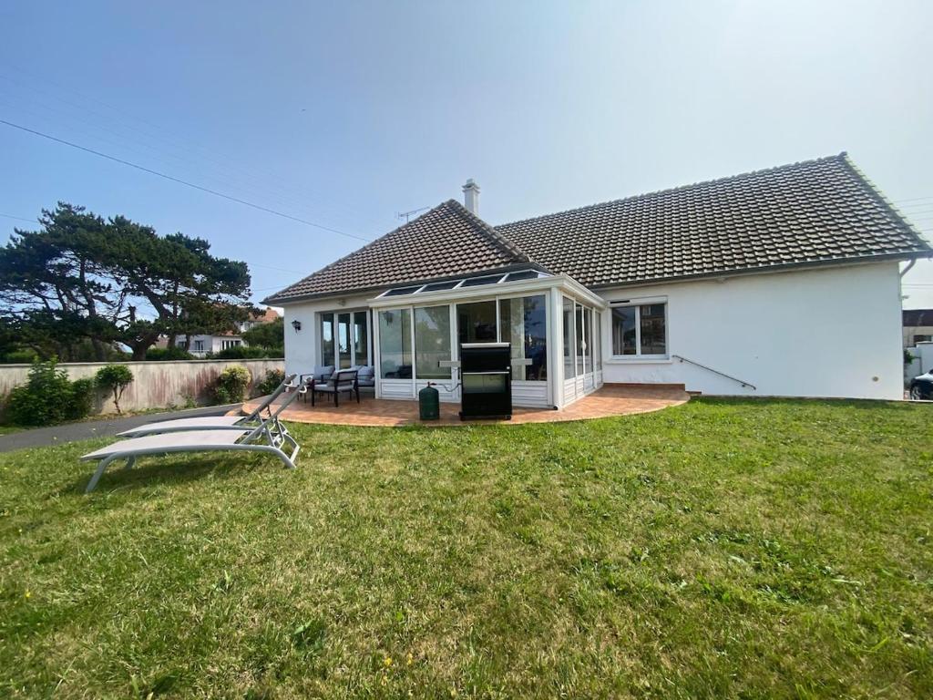 une maison blanche avec une terrasse couverte et une pelouse dans l'établissement Grande Maison familiale 50m de la plage - Le nid d'Asnelles, à Asnelles