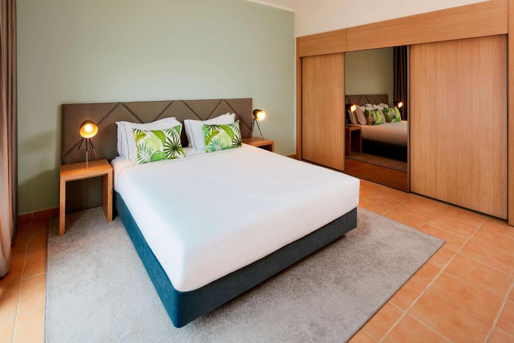 a bedroom with a large white bed and a mirror at NH Marina Portimao Resort in Portimão