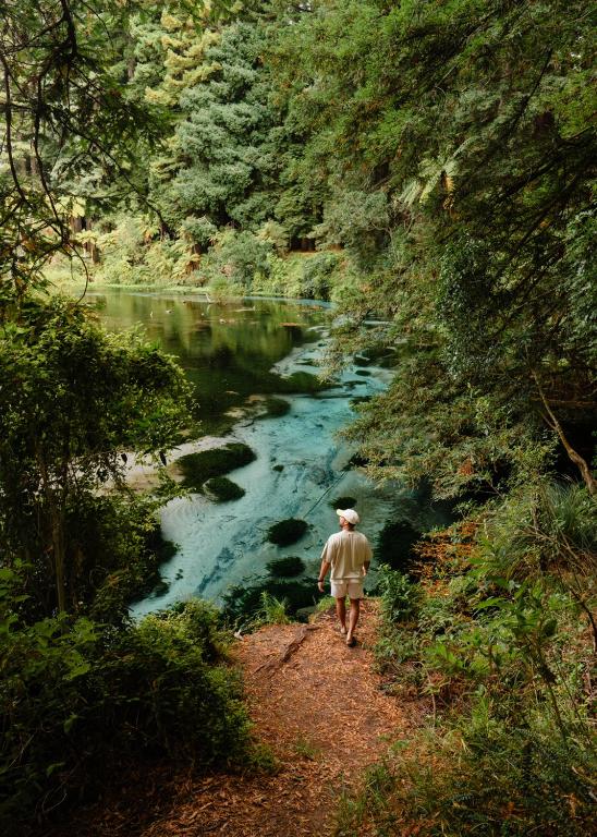 a man walking down a path next to a river at Tasman Holiday Parks - Rotorua in Rotorua