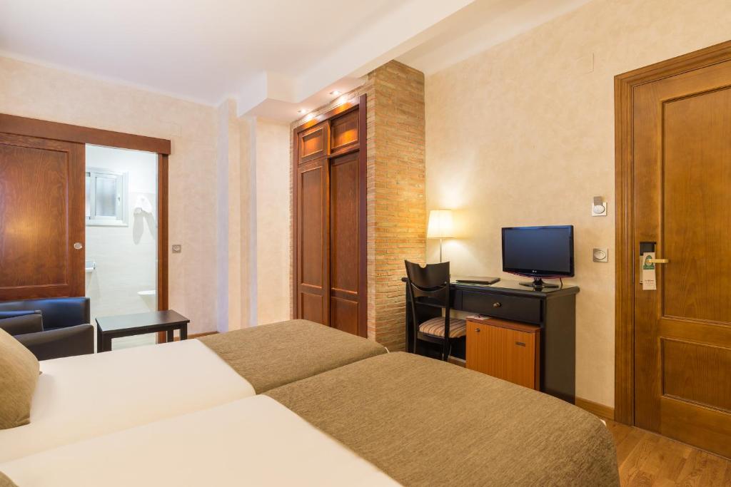 a hotel room with a bed and a desk with a television at BYPILLOW California in Málaga