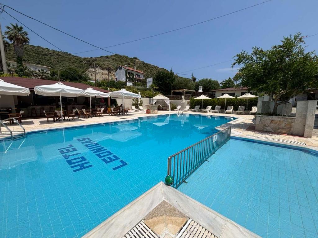 a large blue swimming pool with tables and umbrellas at Leonidas Apartments & Suites 2 in Mola Kalyva