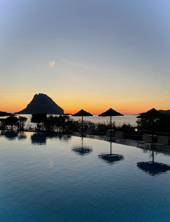 a swimming pool with umbrellas and the ocean at sunset at Hotel Don Diego in Porto San Paolo