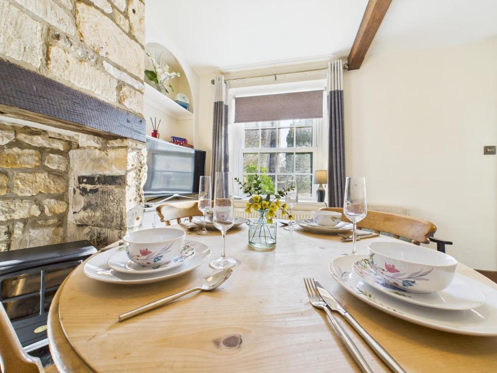 a wooden table with plates and wine glasses on it at Romantic Cottage Cotswolds Parking Wi-Fi in Winchcombe