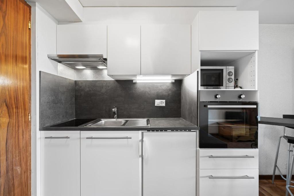 a white kitchen with a sink and a microwave at Arnica 2 - 2 pers - piscine in Nendaz