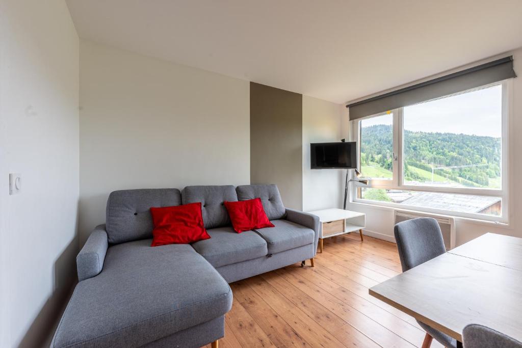 un salon avec un canapé gris avec des coussins rouges dans l'établissement La Belle Evasion - proche station de ski, aux Gets