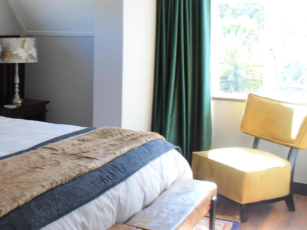 a bedroom with a bed and a chair and a window at Wild Tree Lodge in Benoni