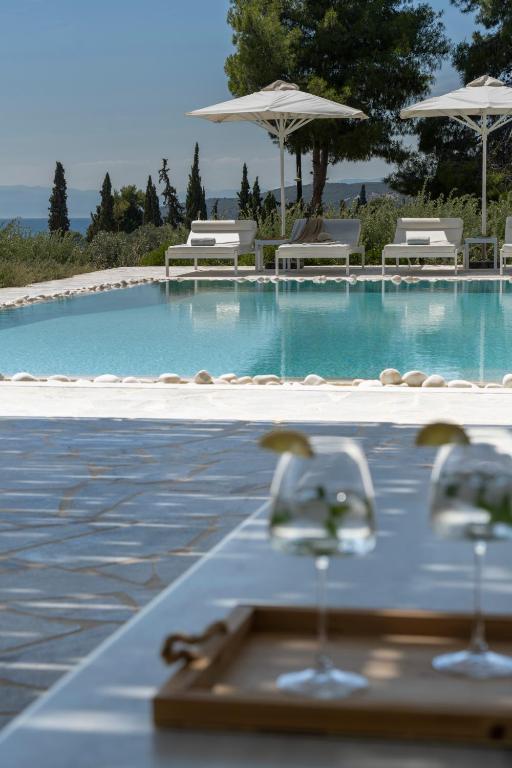 a swimming pool with chairs and a table with wine glasses at Villa Seascape, Beachfront Living in the Greek Riviera Porto Heli in Porto Heli