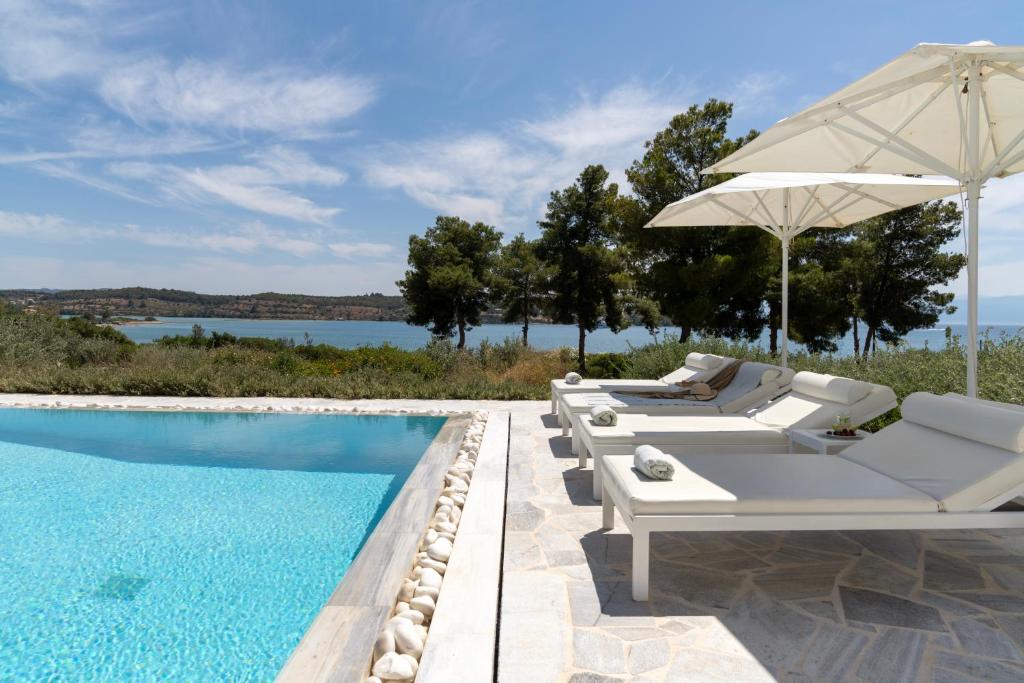a swimming pool with lounge chairs and an umbrella next to a pool at Villa Seascape, Beachfront Living in the Greek Riviera Porto Heli in Porto Heli