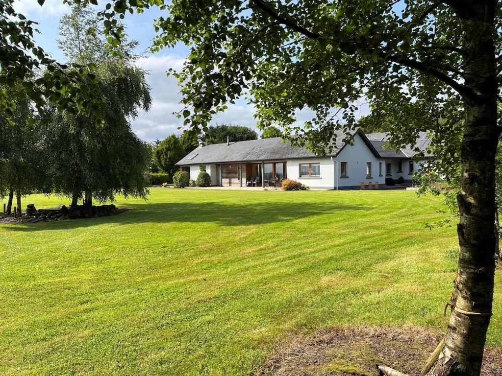 a house in a field with a tree in the foreground at Ballycorrigan Lodge Luxury house for up to 12 guests in Ballina