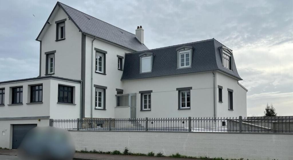 une grande maison blanche avec un toit noir dans l'établissement Villa du homard bleu, à Donville-les-Bains