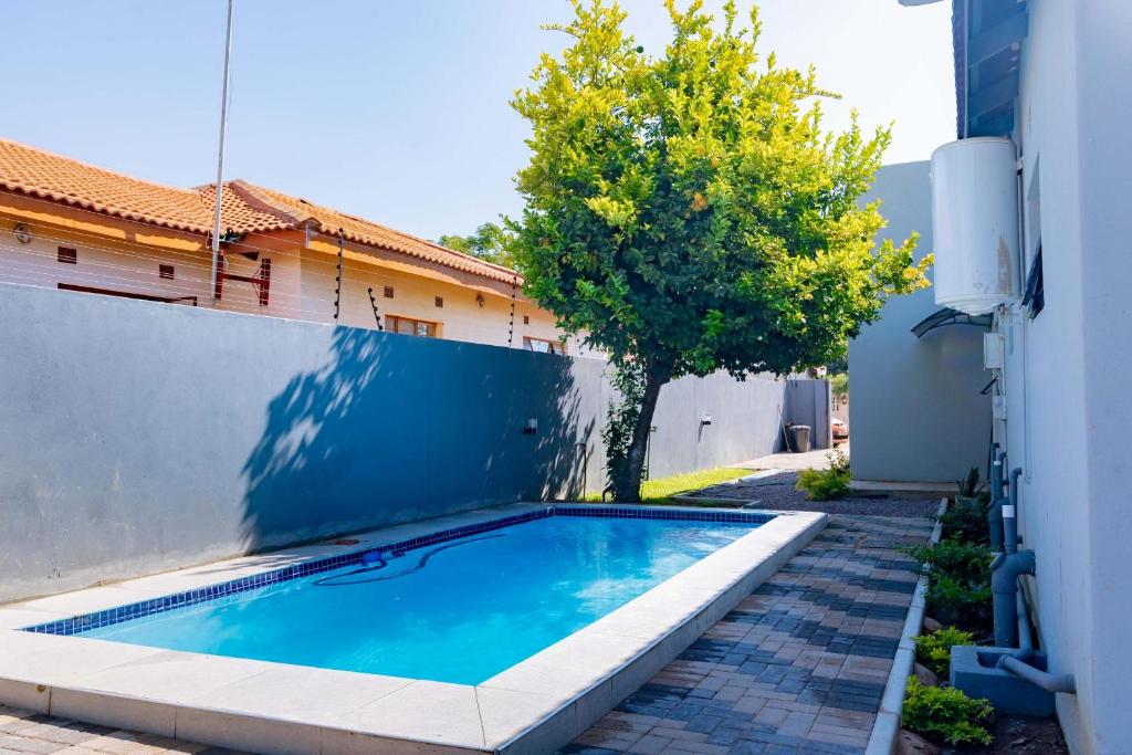 a swimming pool next to a building with a tree at Gaborone City Center stay, ultrafast wifi & near CBD & Airport in Joverega
