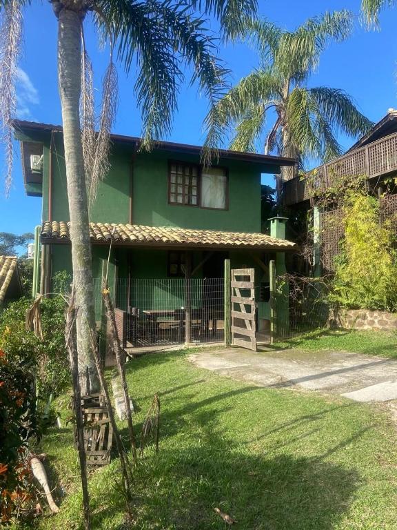 a green house with palm trees in front of it at Pousada vale verde bungalows - Praia do Rosa in Praia do Rosa